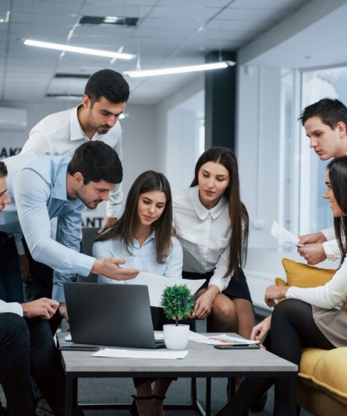 Guy shows document to a girl. Group of young freelancers in the office have conversation and working.
